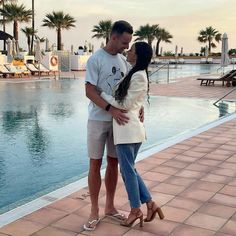 a man and woman standing next to each other near a swimming pool with palm trees in the background