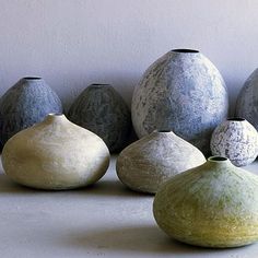 five different colored vases lined up in a row on a table with white wall behind them