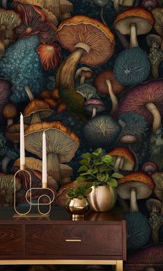 a table with two candles on it next to a wall covered in mushrooms and leaves