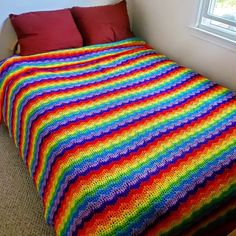 a multicolored crocheted blanket sitting on top of a bed next to a window