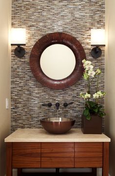 a bathroom vanity with a round mirror above it and flowers in a vase on the counter