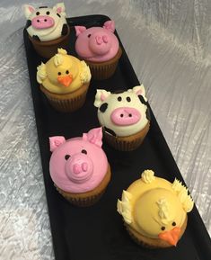 cupcakes with frosting in the shape of farm animals on a black tray