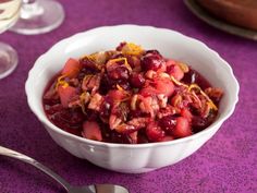 a bowl filled with fruit and nuts on top of a purple table cloth next to silverware