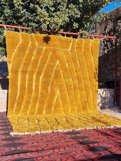 a yellow blanket is hanging on a red metal rack with trees in the back ground