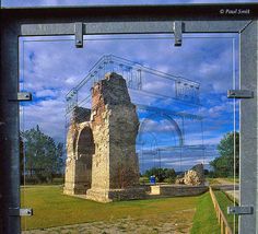 the reflection of an old building in a glass door frame with grass and trees behind it