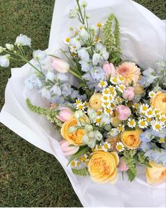 a bouquet of flowers sitting on top of a white wrapper in the grass next to some blue and yellow flowers