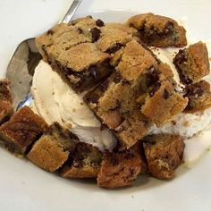 a white plate topped with ice cream and chocolate chip cookie cake squares next to a fork