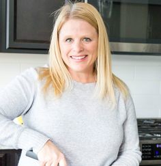 a woman standing in front of a stove holding a knife and cutting food on a board