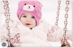 a baby is sitting on a swing wearing a pink teddy bear hat and jacket with ears