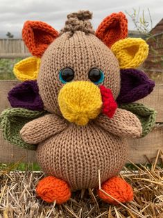 a knitted stuffed turkey sitting on top of some dry grass in front of a fence