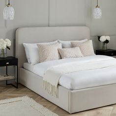 a bed with white linens and pillows in a large room next to a night stand