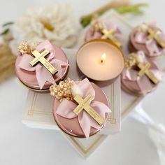 three pink cupcakes with gold crosses on them sitting next to a lit candle