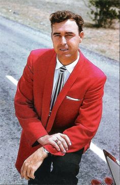 a man in a red suit and tie standing next to a motorcycle on the road