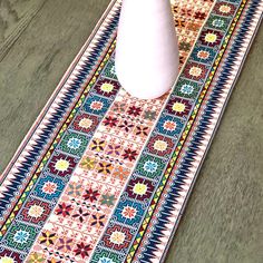 a white vase sitting on top of a table next to a colorful rug and flower pot