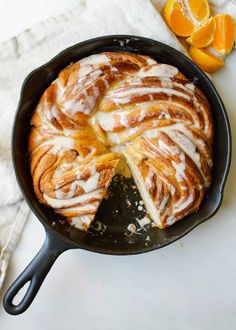 a cinnamon roll in a cast iron skillet on a white table with oranges