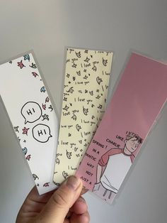 three bookmarks in the shape of cartoon characters are held by a person's hand