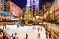 people skating on an ice rink in front of tall buildings and christmas tree at night