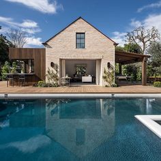 a house with a pool in the foreground and an outdoor dining area on the other side