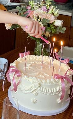 a person lighting candles on a cake with pink ribbon and flowers in the background,