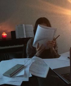 a woman sitting at a desk reading a book and holding a pen in front of her face