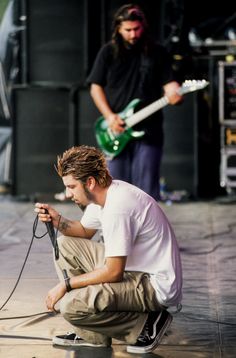 a man sitting on the ground with a microphone in front of him and another person standing behind him