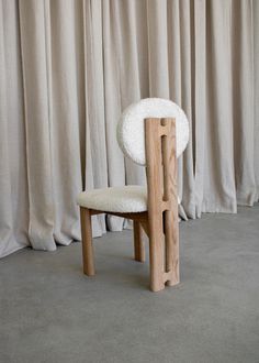 a wooden chair with white sheep fur on it's back and seat, in front of curtained drapes