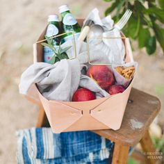 a basket filled with apples sitting on top of a wooden chair next to a tree