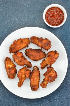 chicken wings on a white plate next to a small bowl of chili condiments