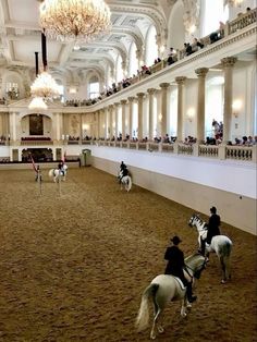 people riding horses in an indoor arena with chandeliers