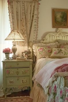 a white bed sitting next to a window covered in curtains and pink flowers on top of it