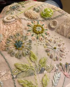 an embroidered pillow with flowers and leaves on it's back side, sitting on a table