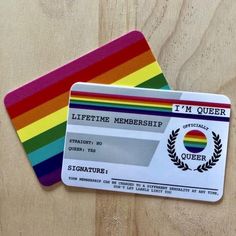 two credit cards sitting next to each other on top of a wooden table with a rainbow stripe