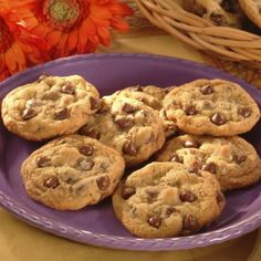 chocolate chip cookies on a purple plate next to orange flowers and wicker basket with pumpkins in the background