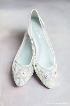 two pairs of white wedding shoes with beading on the bottom and heel, sitting on a gray surface