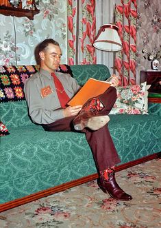 a man sitting on top of a green couch holding an orange book in his hands