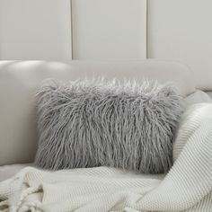 a white bed topped with a fluffy gray pillow