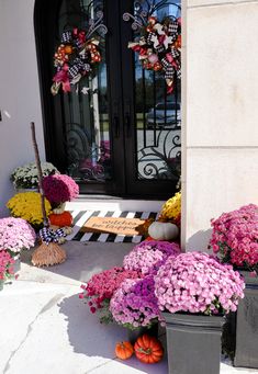 the front door is decorated with flowers and wreaths for halloween decorations, as well as two buckets full of pumpkins