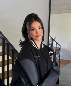 a woman standing in front of a stair case wearing a black jacket with white stripes