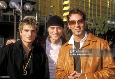 three men standing next to each other in front of a tall building wearing sunglasses and leather jackets