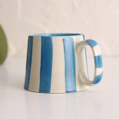 a blue and white striped coffee mug sitting on a table next to an apple in the background