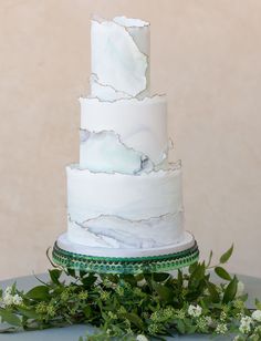 a three tiered white cake sitting on top of a table next to greenery