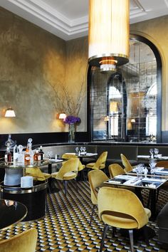 the interior of a fancy restaurant with yellow chairs and black tables in front of an arched window