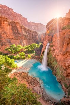 a waterfall in the middle of a canyon with blue water and green trees around it