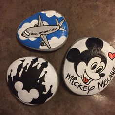 three painted rocks with mickey mouse and an airplane in the sky on top of them