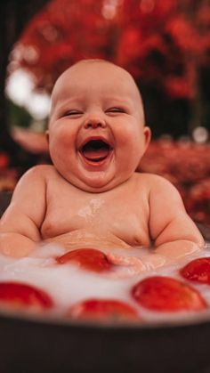 a laughing baby in a bathtub with tomatoes on the bottom and water running down it's face