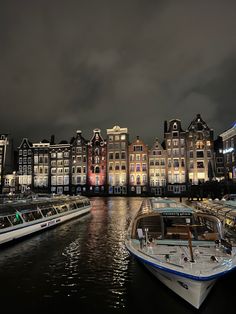 several boats are docked on the water in front of some buildings and lights at night