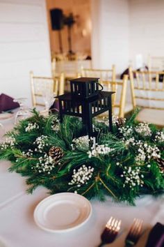 an arrangement of greenery and candles sits on a table at a wedding reception with gold chairs