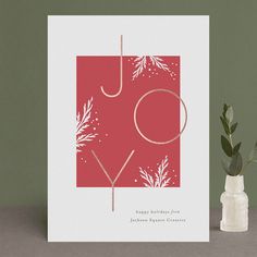 a red and white holiday card with the word joy on it next to a plant