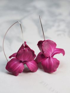 two pink flowers are hanging from silver hoop earrings on a marble surface with white background