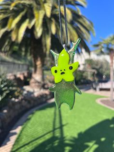 a green toy hanging from a string in front of a palm tree and grass area